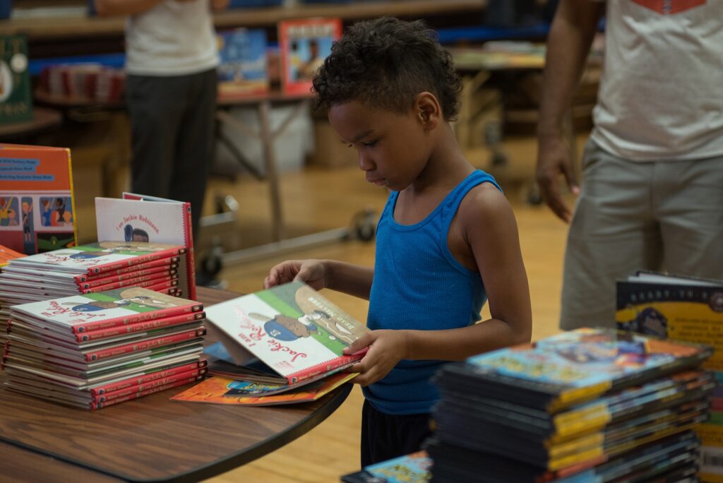 Black boy in blue shirt reading the cover of a book at a book giveaway