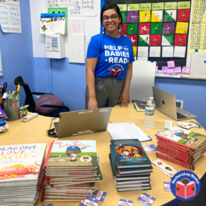 Woman standing in front of a desk with books on it smiling at a book giveaway event.